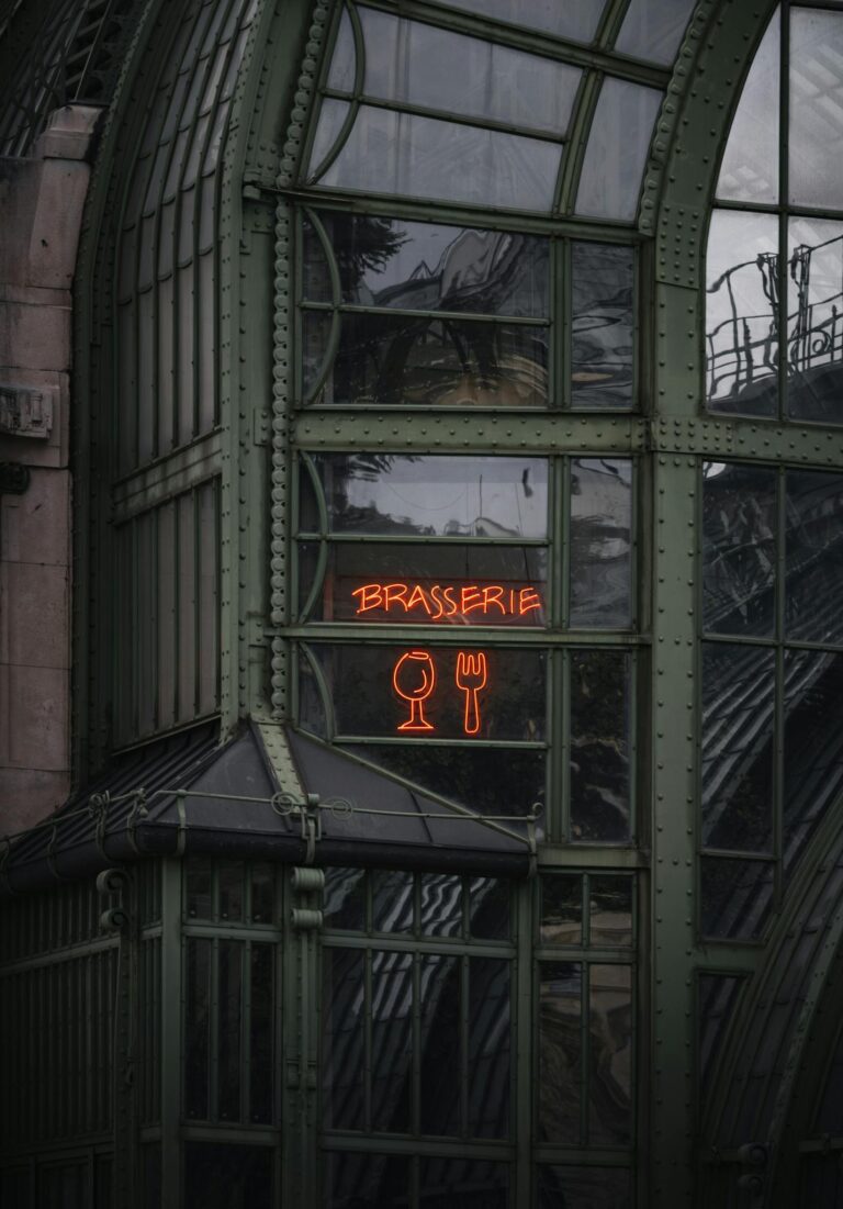 A neon brasserie sign on a historic green metal and glass building in Vienna.